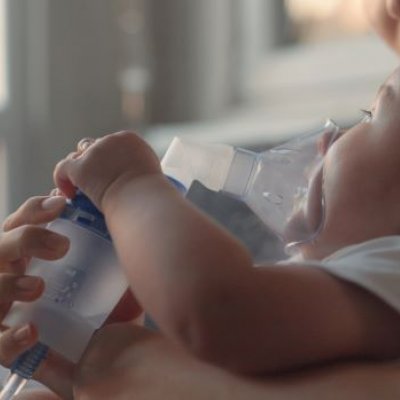 Child lying on bed with nebuliser mask on face.